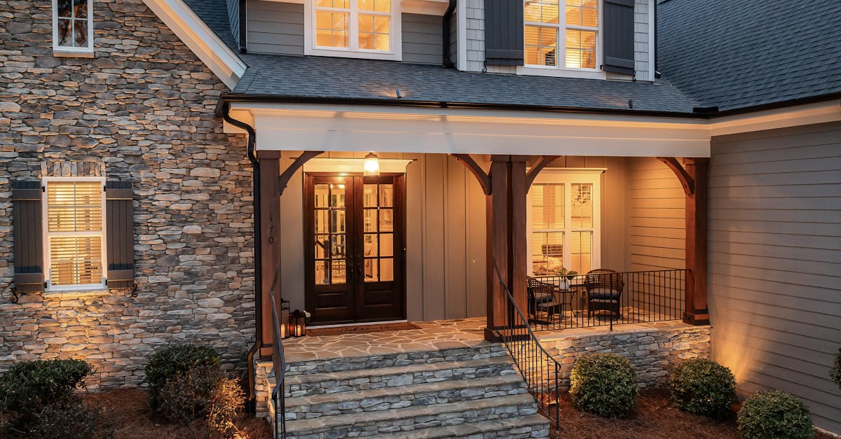 Inviting front porch of a cozy house with stone facade and warm lighting at dusk.